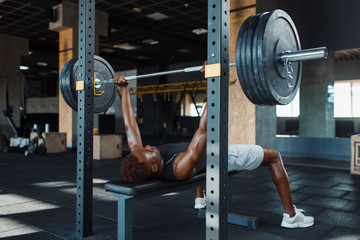 Muscular man doing exercise with barbell in gym