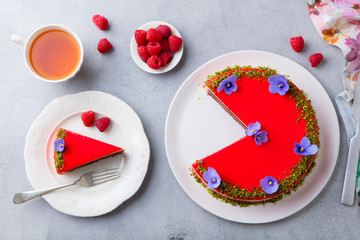 Raspberry layerd cake decorated with violet flowers and tea cup. Grey stone background. Top view.