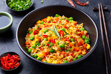 Asian fried rice with egg and vegetables. Dark stone background. Close up.