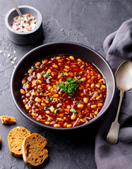 Bean soup in a black bowl. Dark background. Close up.