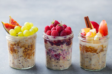 Assortment overnight oats, bircher muesli with fresh berries and fruits in a glass jars. Grey...