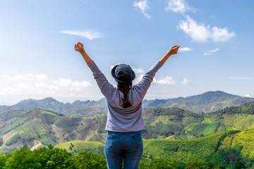 Women with backpacks and hat spreading hands feelings happy and relaxing with nature mountain background. Freedom concept travel in Thailand.