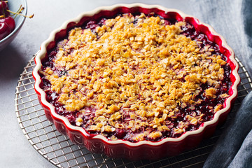 Cherry, red berry crumble in baking dish. Grey stone background. Close up.