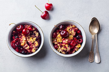 Cherry, red berry crumble in bowl. Grey stone background. Top view.