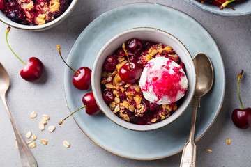 Cherry, red berry crumble with ice cream in bowl. Grey stone background. Top view.