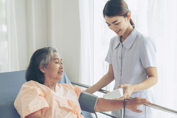 nurse measuring blood pressure of senior elderly woman in hospital bed patients - medical and healthcare senior concept