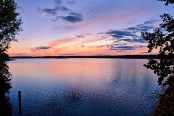 View of the lake at sunset with picturesque play of colors, silhouettes and a peaceful atmosphere.
