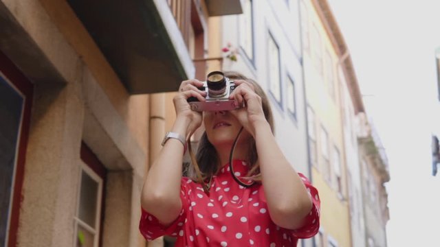Young pretty woman, blogger, traveler, is taking a photo on her vintage camera, exploring portuguese culture, having great time in Portugal, successful and happy, Slow motion.
