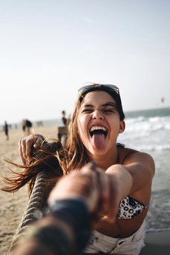 PORTRAIT OF YOUNG WOMAN STICKING OUT TONGUE ON BEACH