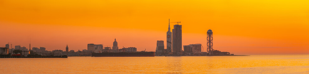 Batumi, Adjara, Georgia. Skyline Of Resort Town At Sunset Sunrise. Bright Orange Evening Sky. View From Sea To Cityscape With Modern Urban Architecture, Skyscrapers And Tower. Golden Hour. Panorama