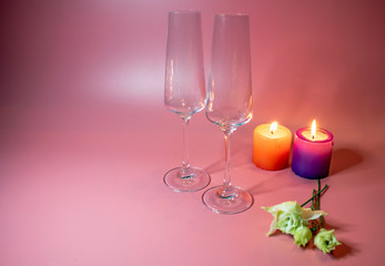 Crystal glasses and two bright red hearts as a symbol of love on the background of candles.