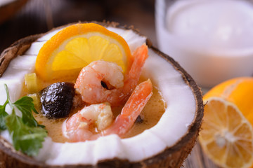 Delicious Soup tom yam in a coconut with shrimps and mushroom on a wooden table next to slice of lemon