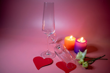 Crystal glasses and two bright red hearts as a symbol of love on the background of candles.