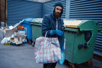 Male bearded beggar searching food in trashcan