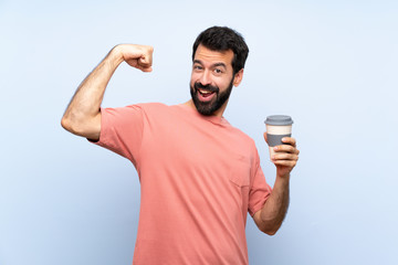 Young man with beard holding a take away coffee over isolated blue background doing strong gesture