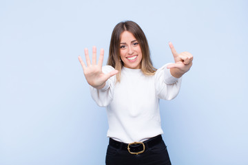 young pretty hispanic woman smiling and looking friendly, showing number seven or seventh with hand...