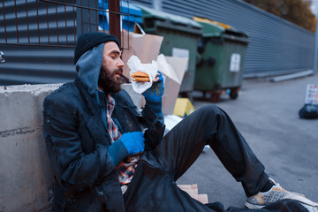 Dirty beggar with food sitting at the trashcan
