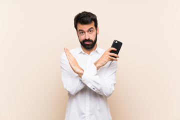 Young man with beard holding a mobile making NO gesture