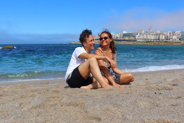 Pareja de un hombre y una mujer sentados en la arena de la playa sonriendo