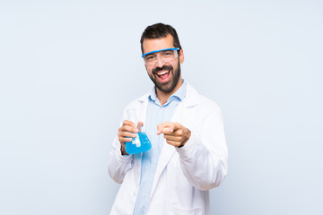 Young scientific holding laboratory flask over isolated background pointing to the front and smiling