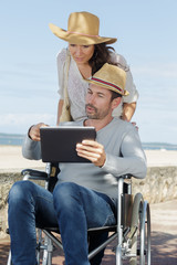 couple by beach looking at tablet man in wheelchair
