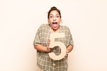 young pretty woman surprised, shocked, amazed, holding a number 5.