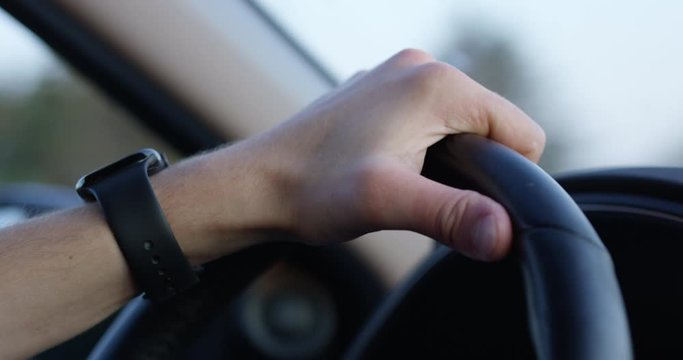 Man hand holding steering wheel in car as he drives - close up on one hand on wheel