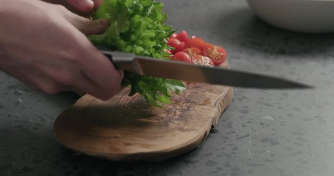 Slow motion man hand cutting frisee sald leaves on olive wood board