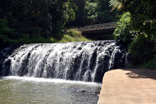 A close up view of the Malanda Falls with a road bridge behind