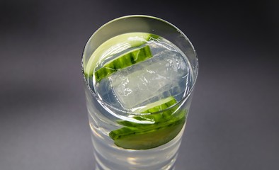 Top view on isolated glass with sparkling tonic water, cucumber slices, gin and ice cubes, white...