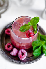 Delicious and refreshing cocktail for summer party. Raspberry syrup, soda, ice, pepper mint. Frozen berries as decor. Bartender equiment on background. Close up, white background