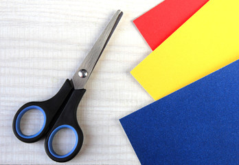 Top view of sheets of colored paper and scissors on light wooden background.