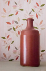 Clay vase in the form of a bottle standing on a background depicting plants. Background