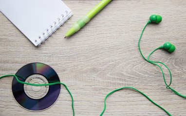 Flat Lay. Green headphones, disk, pure white notebook with rings, green pen are on beige wooden background