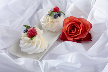 Dessert Pavlova with raspberries, blueberries and mint on a white fabric.