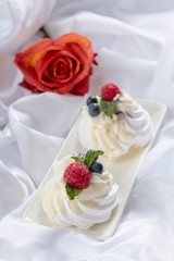 Dessert Pavlova with raspberries, blueberries and mint on a white fabric.