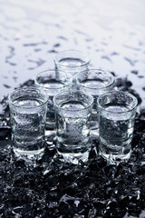 Damp glasses of vodka with ice on a black reflective background.