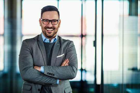 Portrait of a smiling businessman. Portrait of cheerful businessman with arms folded standing in conference room. Happy young business man looking at camera. Portrait of a smiling businessman