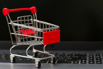 Small shopping cart on silver laptop with black screen background. Online shopping