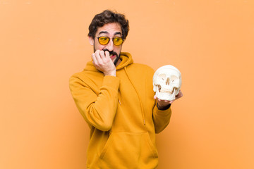 young crazy cool man holding a human skull model against orange wall