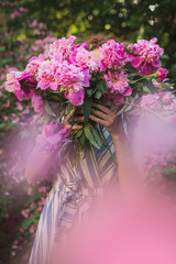 Romantic pretty woman closed face by peonies bouquet in spring blossom garden. Enigma woman. No face