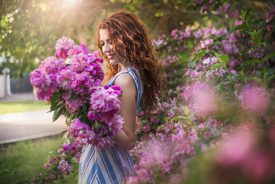 Close up romantic portrait of beautiful young woman in blossom spring garden with bouquet of peonies