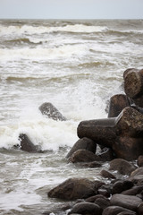 Waves crushing through concrete blocks near path to ship lighthouse in Baltic Sea.