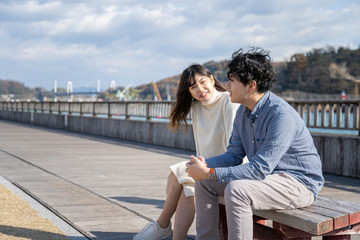 ベンチに座り楽しそうに会話をする若いカップル Wall Mural West Photo