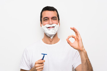 Man shaving his beard over isolated white background showing ok sign with fingers