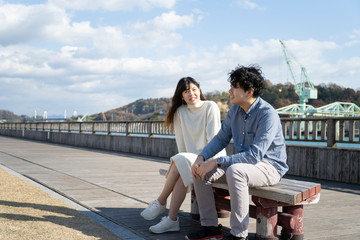 ベンチに座り楽しそうに会話をする若いカップル Wall Mural West Photo