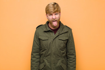 young blonde man feeling disgusted and irritated, sticking tongue out, disliking something nasty...