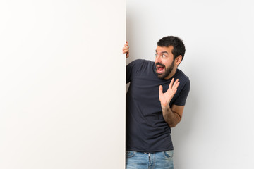 Young handsome man with beard holding a big empty placard nervous and scared