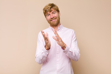 young blonde man feeling happy and successful, smiling and clapping hands, saying congratulations...