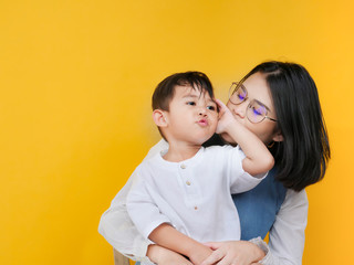Loving mother and son hugging in studio over yellow background.
